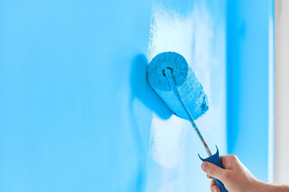 Person using a roller to paint a wall blue